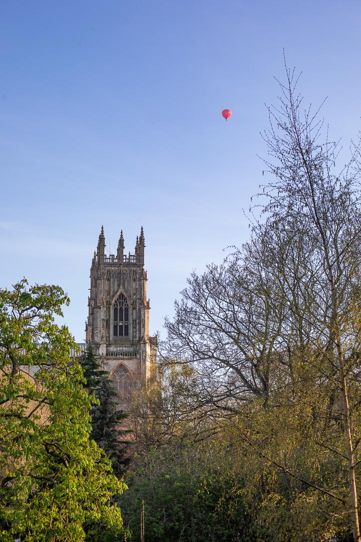 A red hot air balloon high in the sky over York Minster
